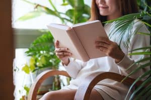 A young woman reading book on balcony with houseplants garden at home